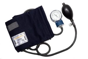 An image of a sphygmomanometer. It has an armband, tubing that connects the armband to an egg-shaped hand-powered air pump, and an analog display that measures blood pressure.